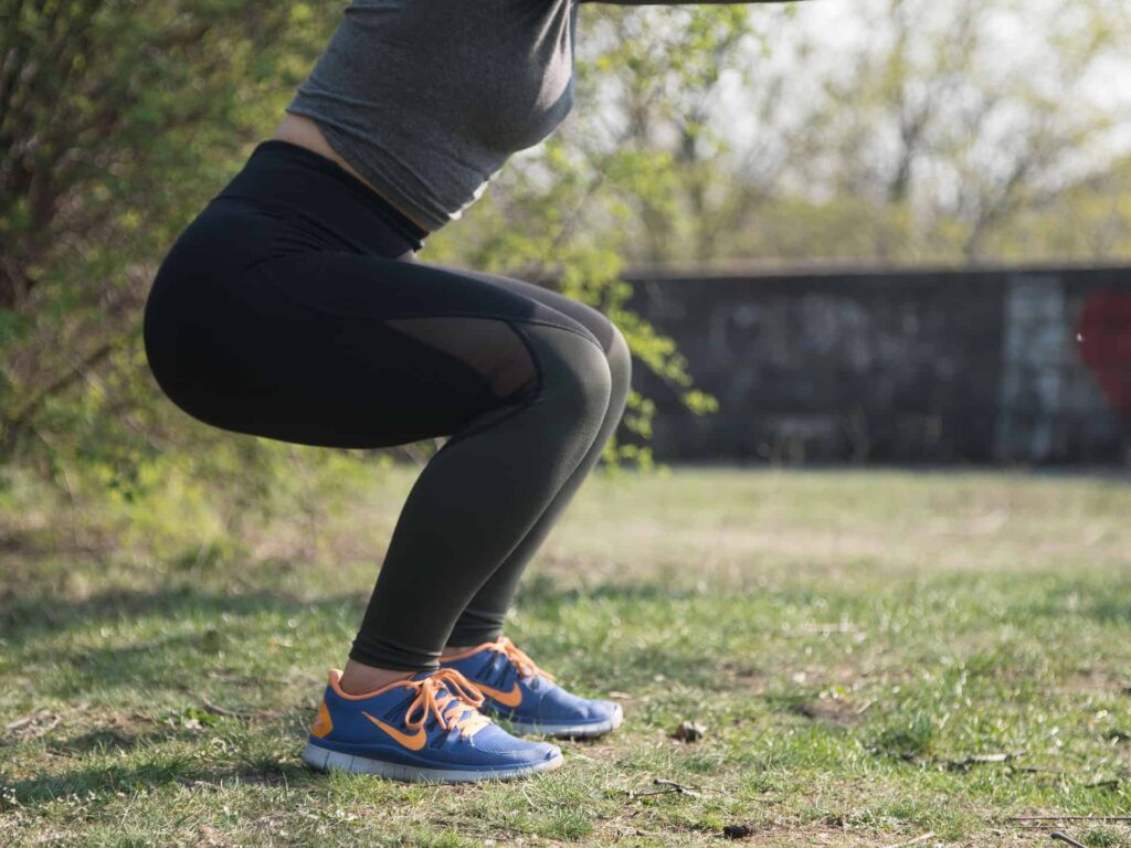 Person performing outdoor squat exercise on grass Person doing a squat outside on grass wearing black leggings, gray top, and blue-orange sneakers