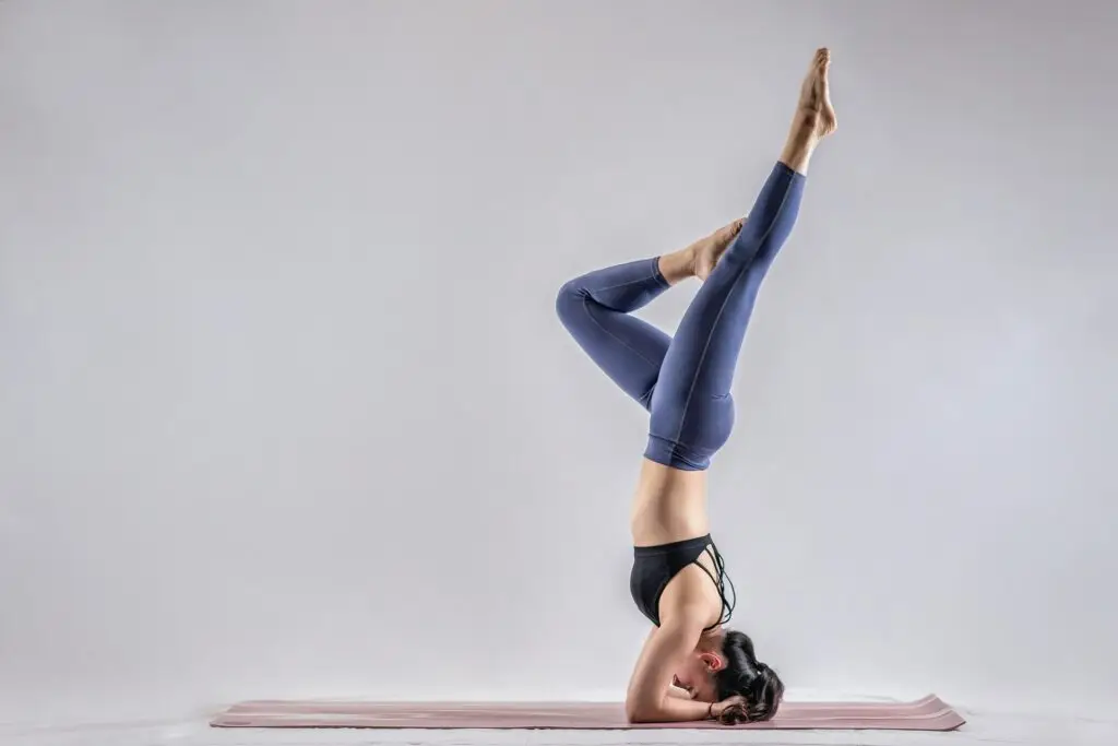 A woman in a handstand position on a yoga mat, demonstrating flexibility and focus during her yoga practice.