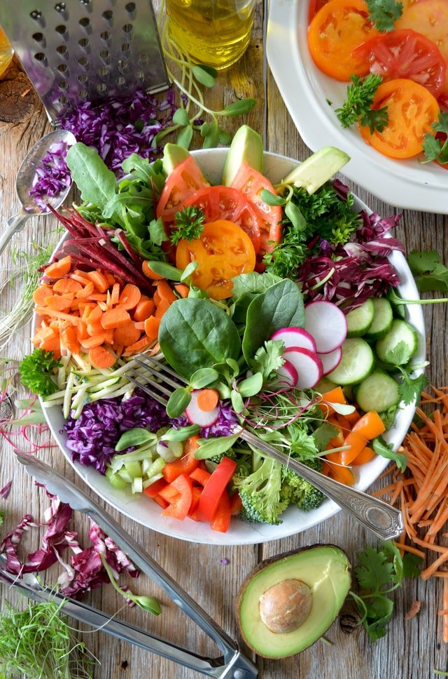 A bowl filled with vibrant vegetables alongside a sharp knife on a wooden cutting board.