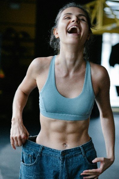 A woman joyfully laughs while holding her jeans, celebrating her transformation after seven days of fasting.